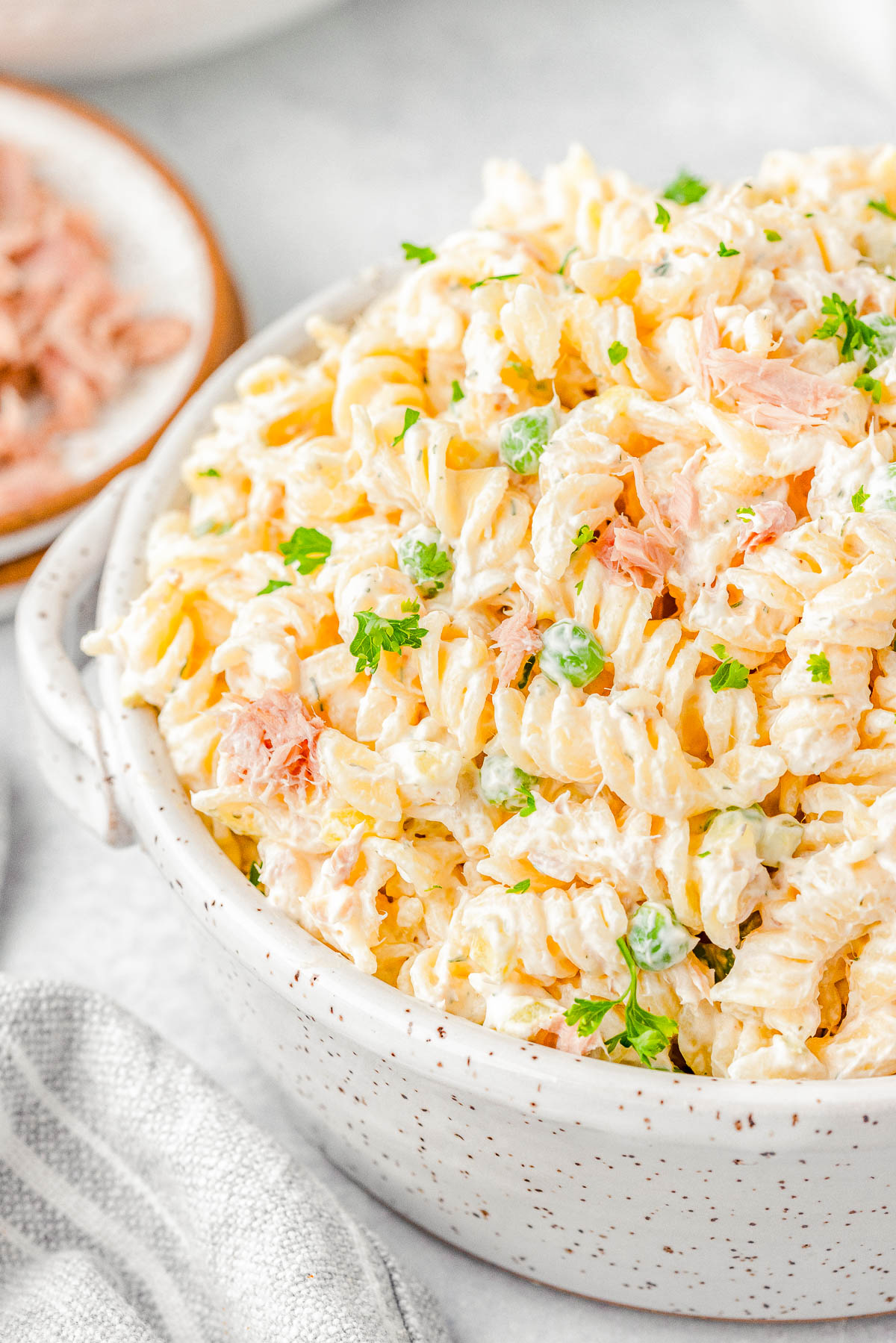 A bowl of creamy pasta salad with rotini noodles, topped with bits of ham and garnished with fresh parsley.