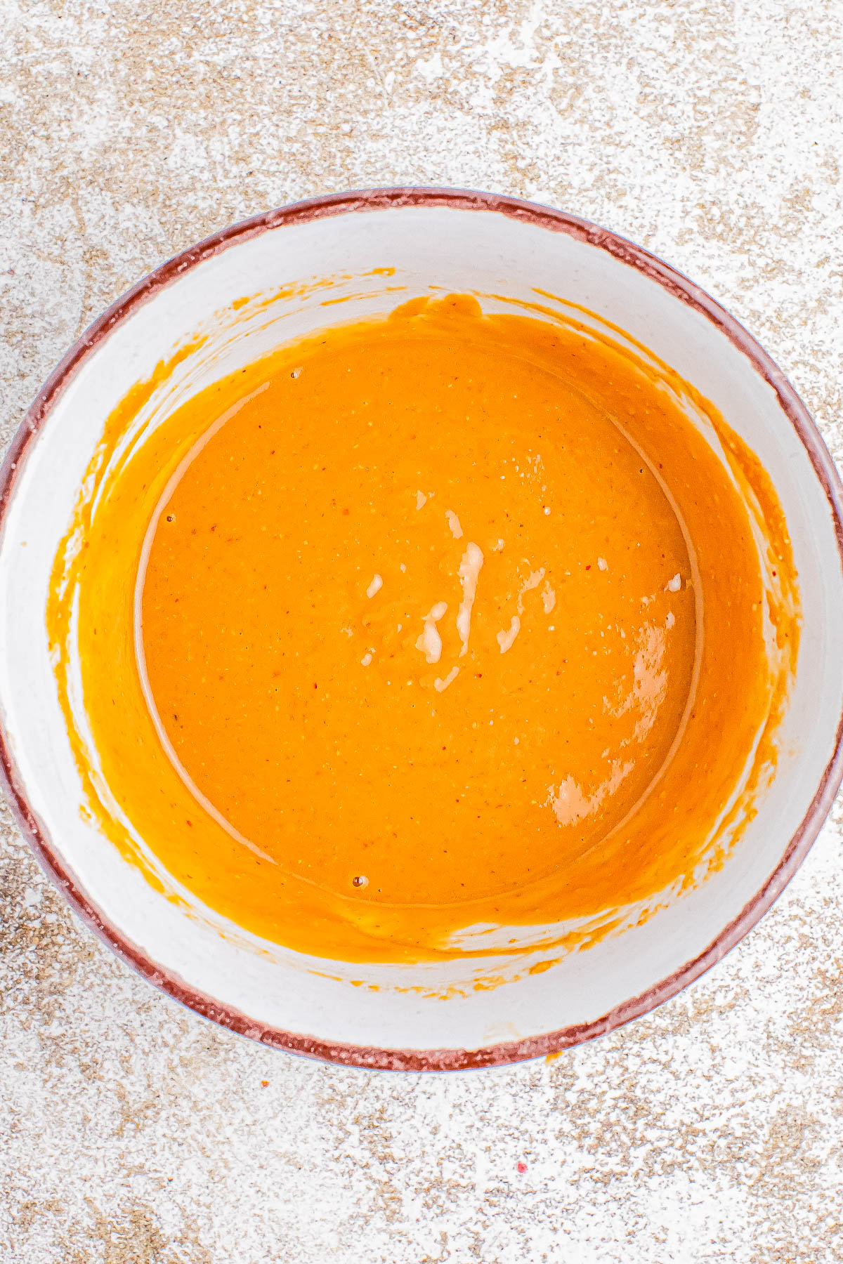 A bowl filled with a smooth, orange batter on a lightly floured surface.