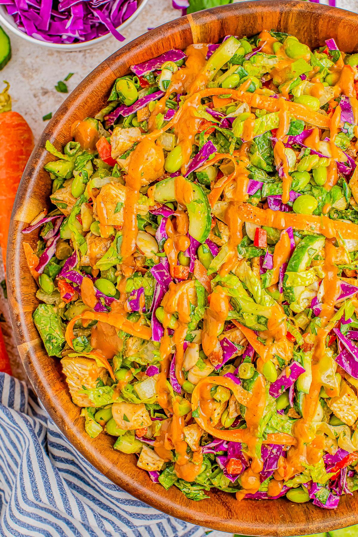 A vibrant salad in a wooden bowl featuring mixed greens, edamame, red cabbage, cucumbers, and carrots, topped with a drizzle of orange dressing.
