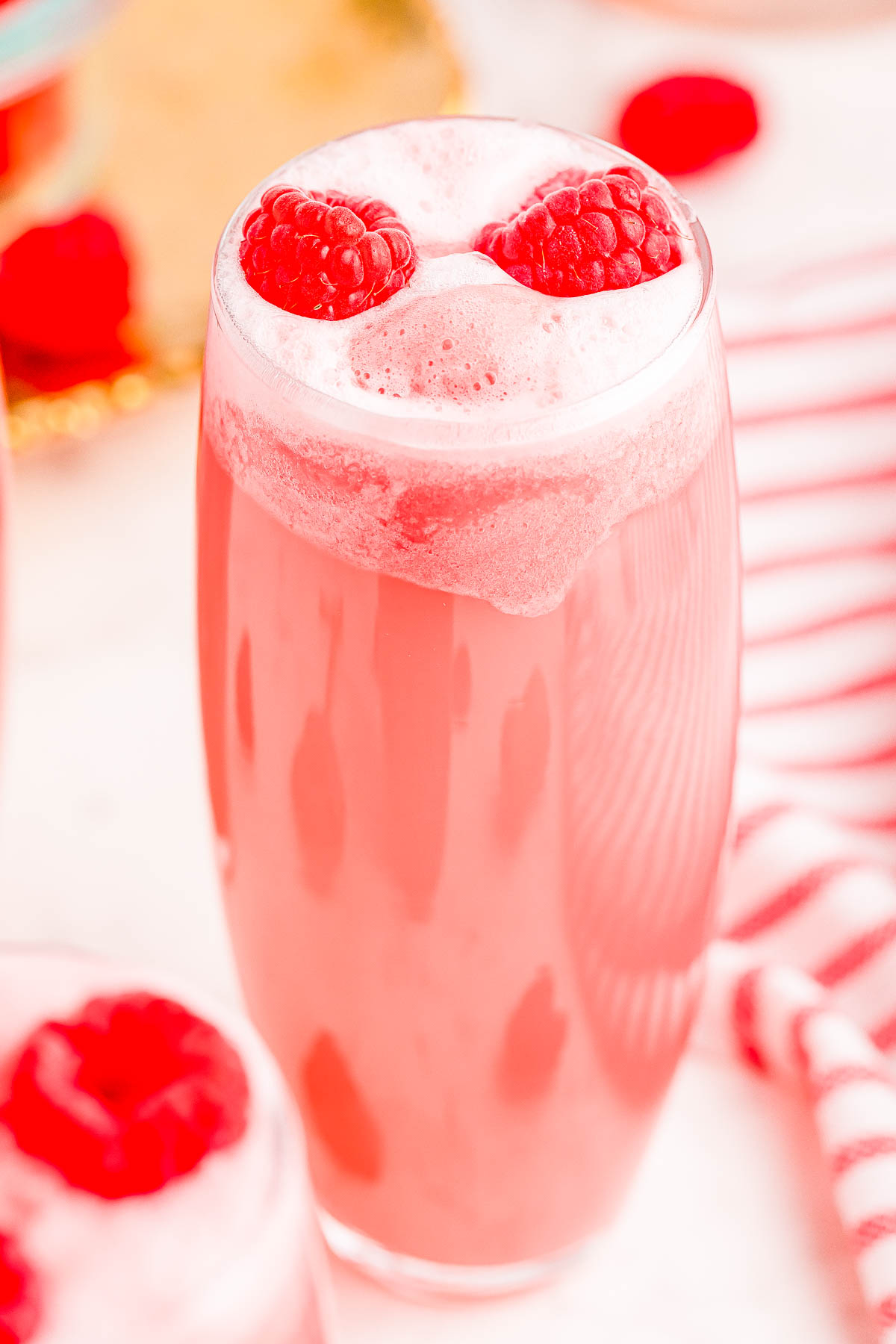 A tall glass filled with a frothy pink drink is topped with two raspberries.