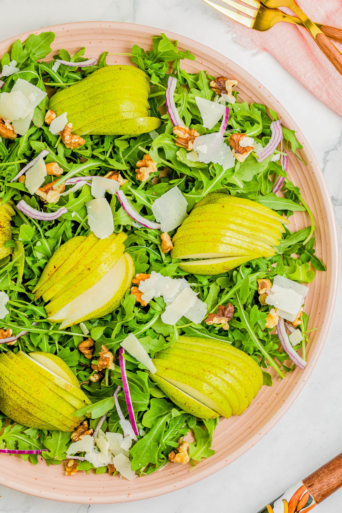 A salad with arugula, sliced pears, walnuts, red onion, and shaved Parmesan cheese on a pink plate.