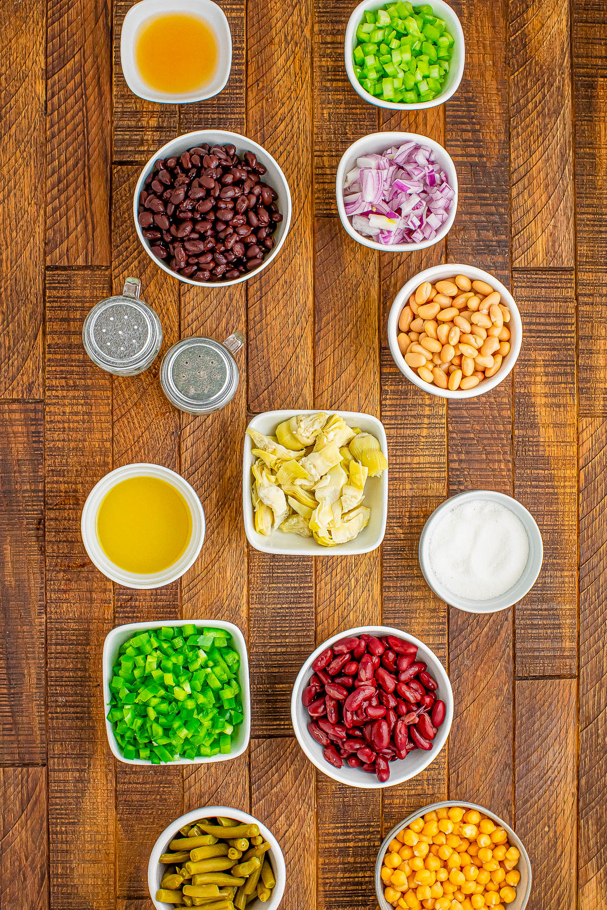 Assorted bowls of ingredients on a wooden surface, including beans, chopped vegetables, liquids, and seasonings, arranged in a neat grid pattern.