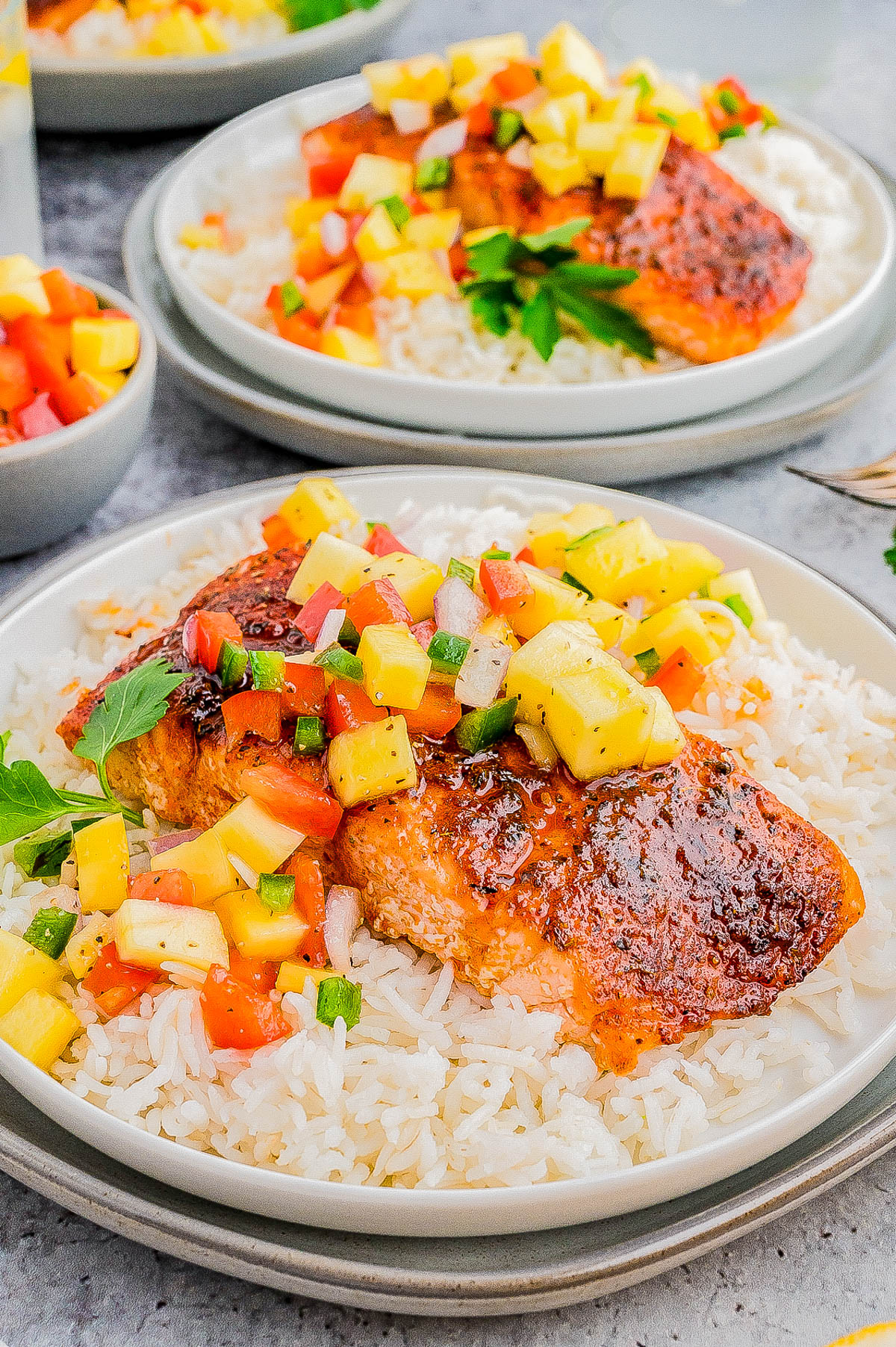 Plates of grilled salmon topped with diced mango salsa served over white rice.