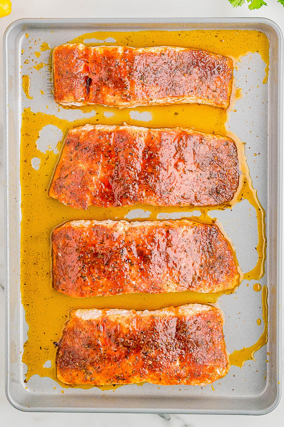 Four pieces of seasoned, cooked salmon fillets on a baking sheet, with a glossy, caramelized finish.