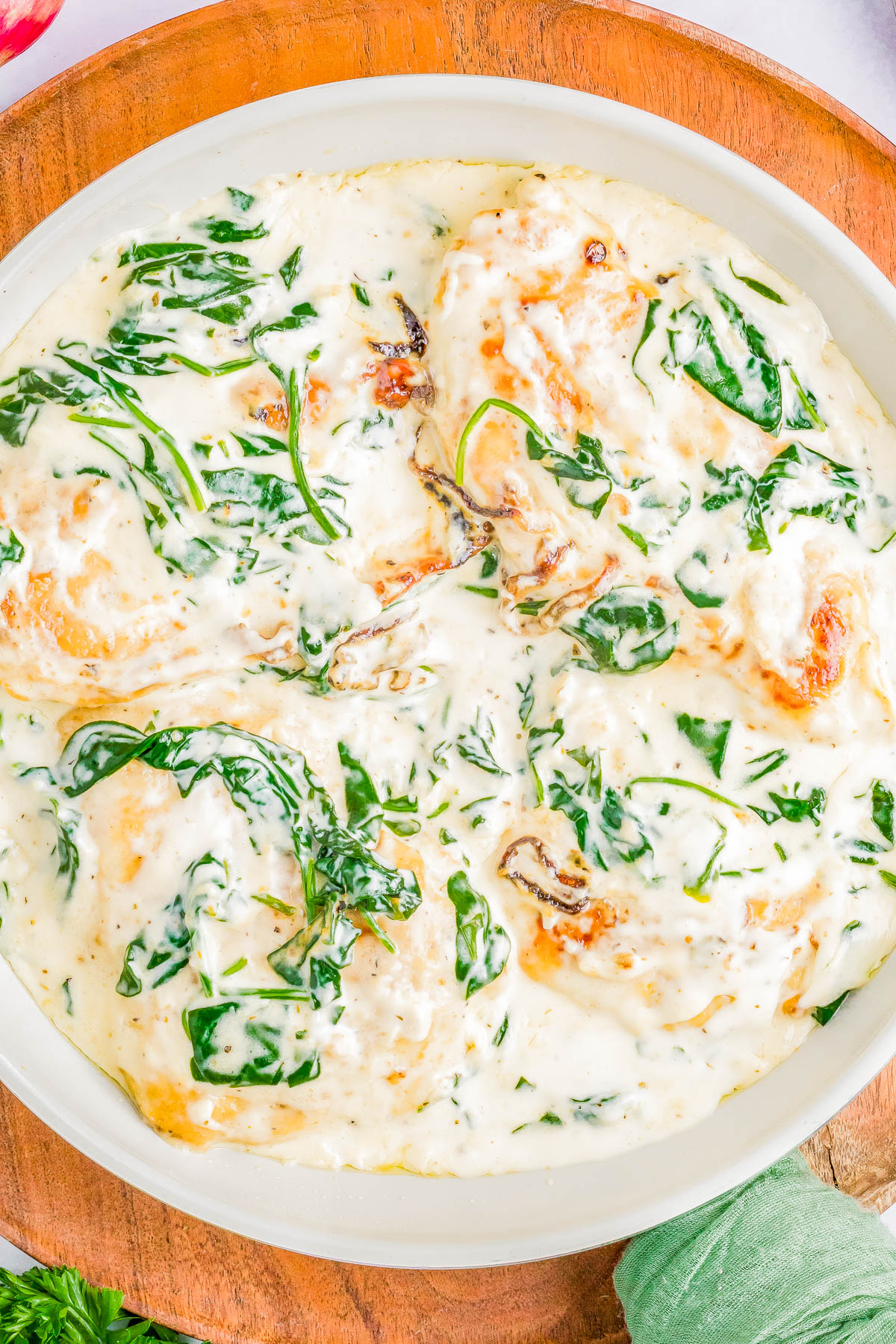 A dish featuring chicken breasts in a creamy white sauce with spinach leaves, served on a round white plate on a wooden surface.