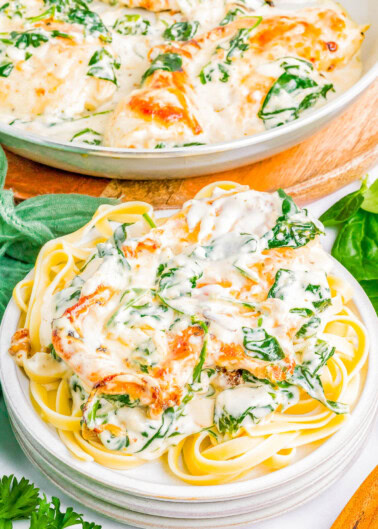 Plate of fettuccine pasta topped with a creamy spinach and cheese sauce, garnished with herbs. A serving dish of the same sauce is in the background.