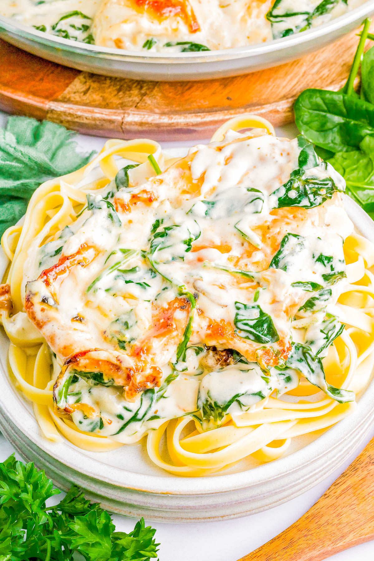 A plate of fettuccine pasta topped with creamy sauce, spinach, and sun-dried tomatoes. Fresh herbs are placed around the dish on the table.