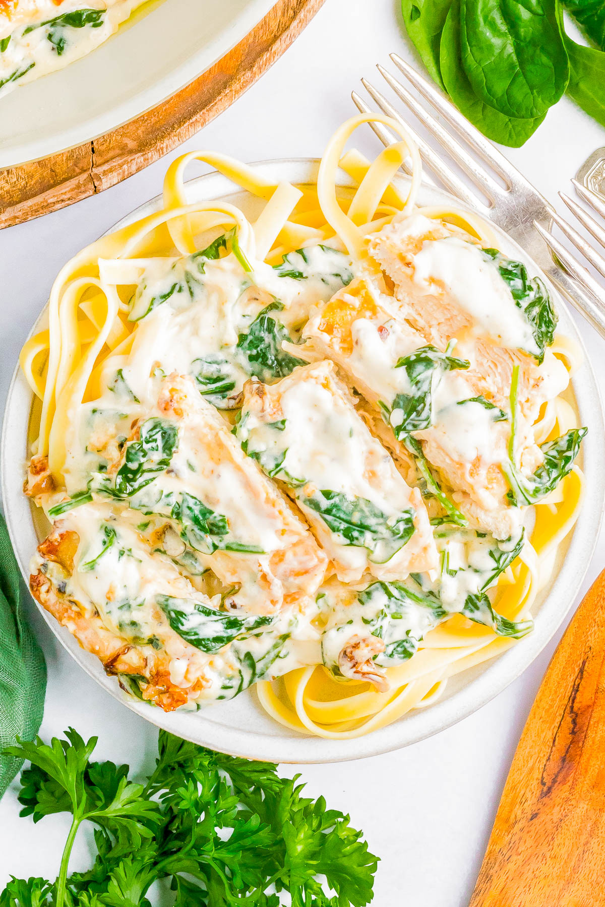 A plate of fettuccine pasta topped with sliced chicken breast and a creamy spinach sauce, garnished with fresh parsley, next to a fork and knife.