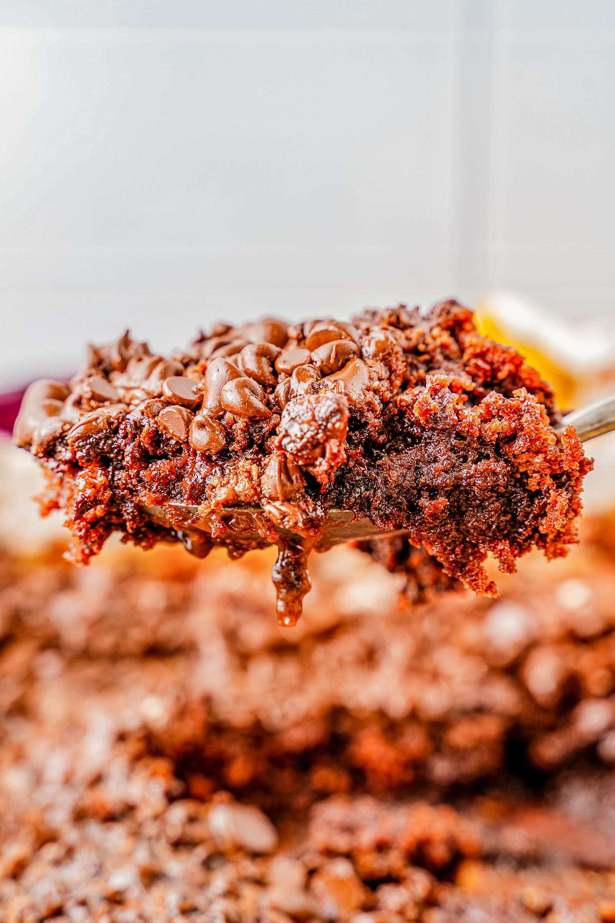 Close-up of a spoon lifting a portion of rich, gooey chocolate cake with melted chocolate chips.