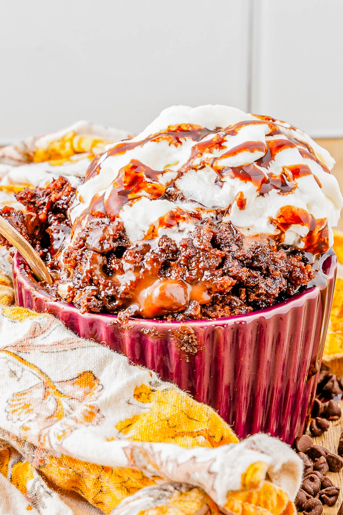 A bowl of chocolate dessert topped with whipped cream and chocolate syrup, placed on a patterned cloth napkin.