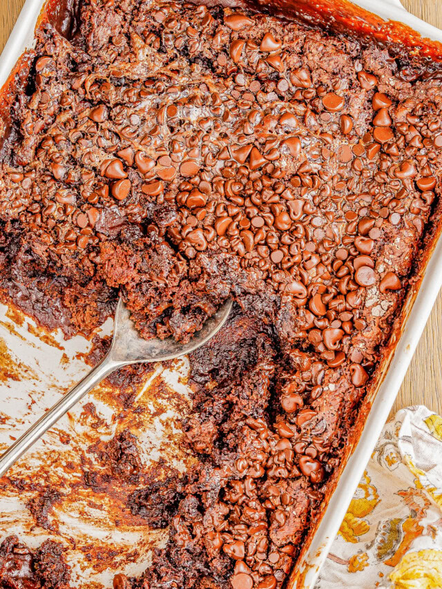 A baking dish filled with chocolate molten lava cake, topped with melted chocolate chips, partially scooped out with a large spoon.