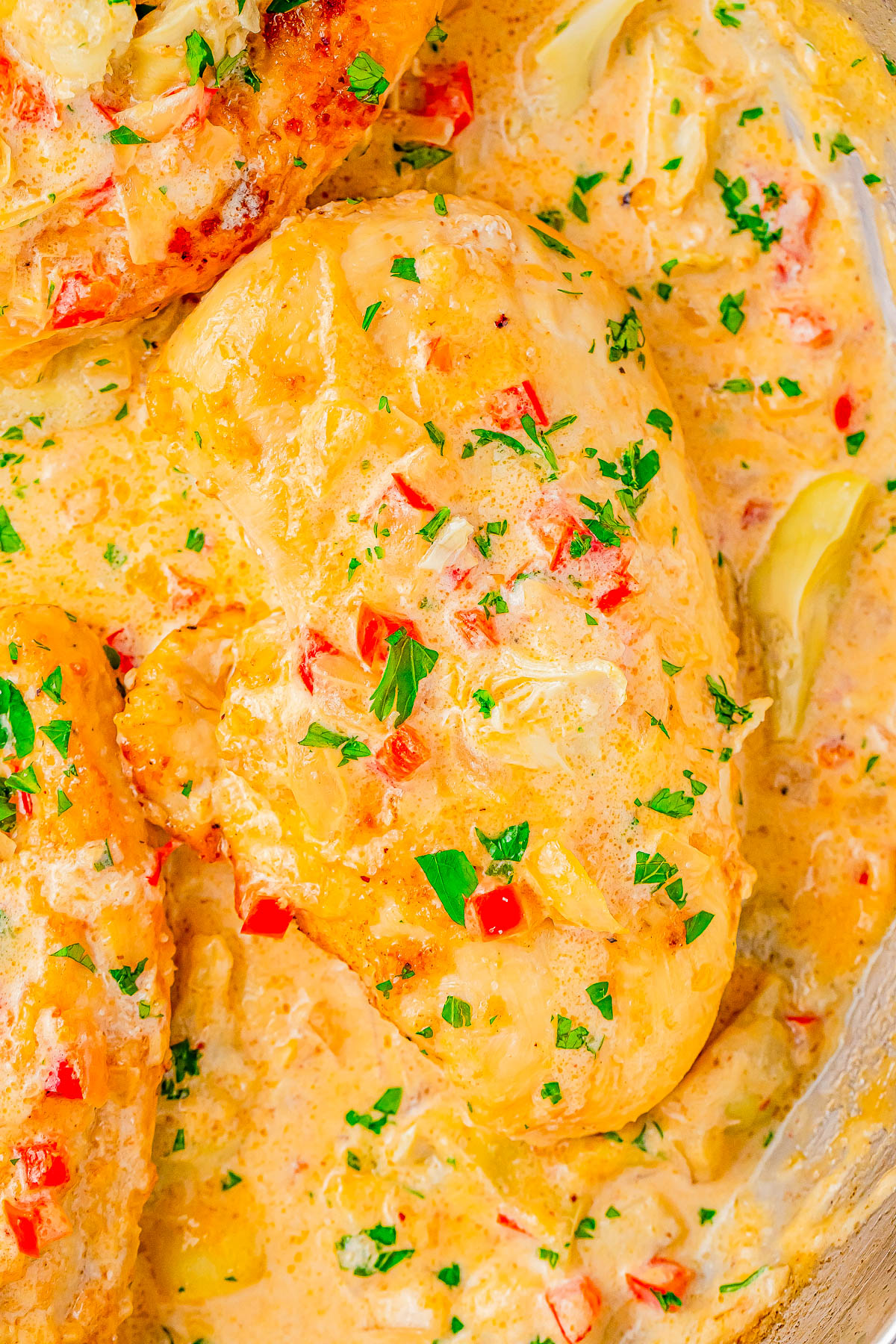 Close-up of chicken breasts cooked in a creamy sauce with diced red bell peppers and garnished with chopped parsley.