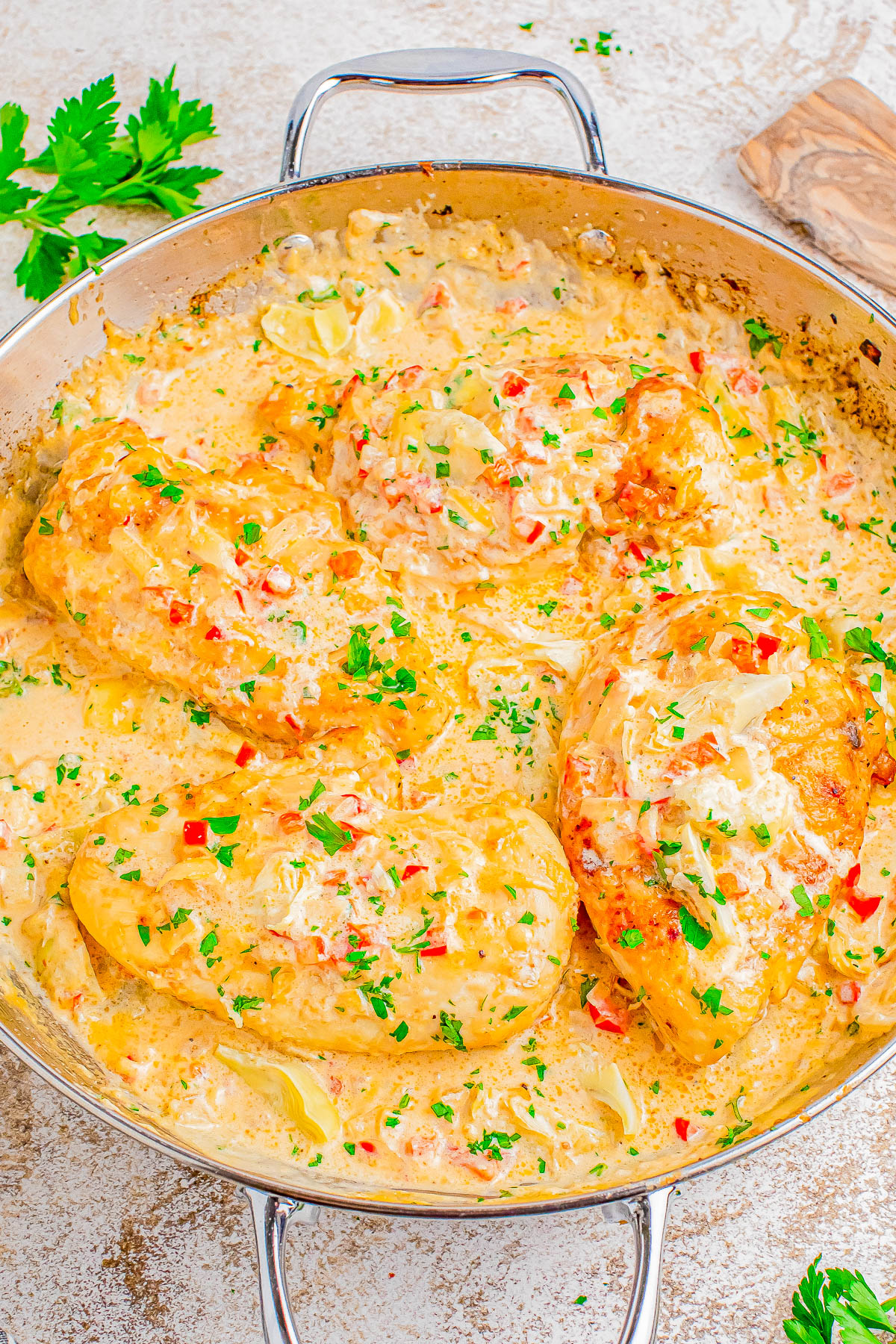 Creamy garlic chicken breasts garnished with chopped parsley in a skillet.