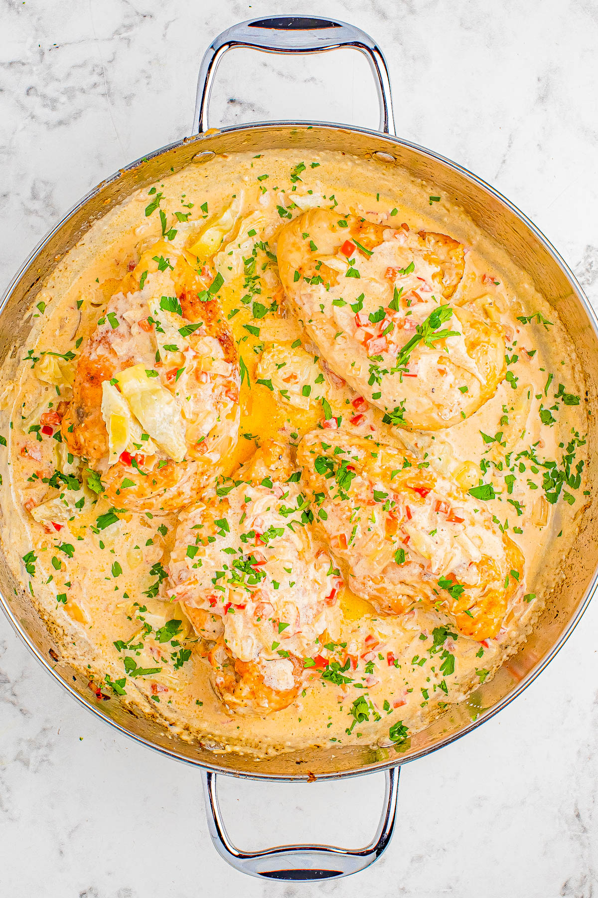 A pan filled with creamy garlic parmesan chicken garnished with chopped parsley, on a marble countertop.