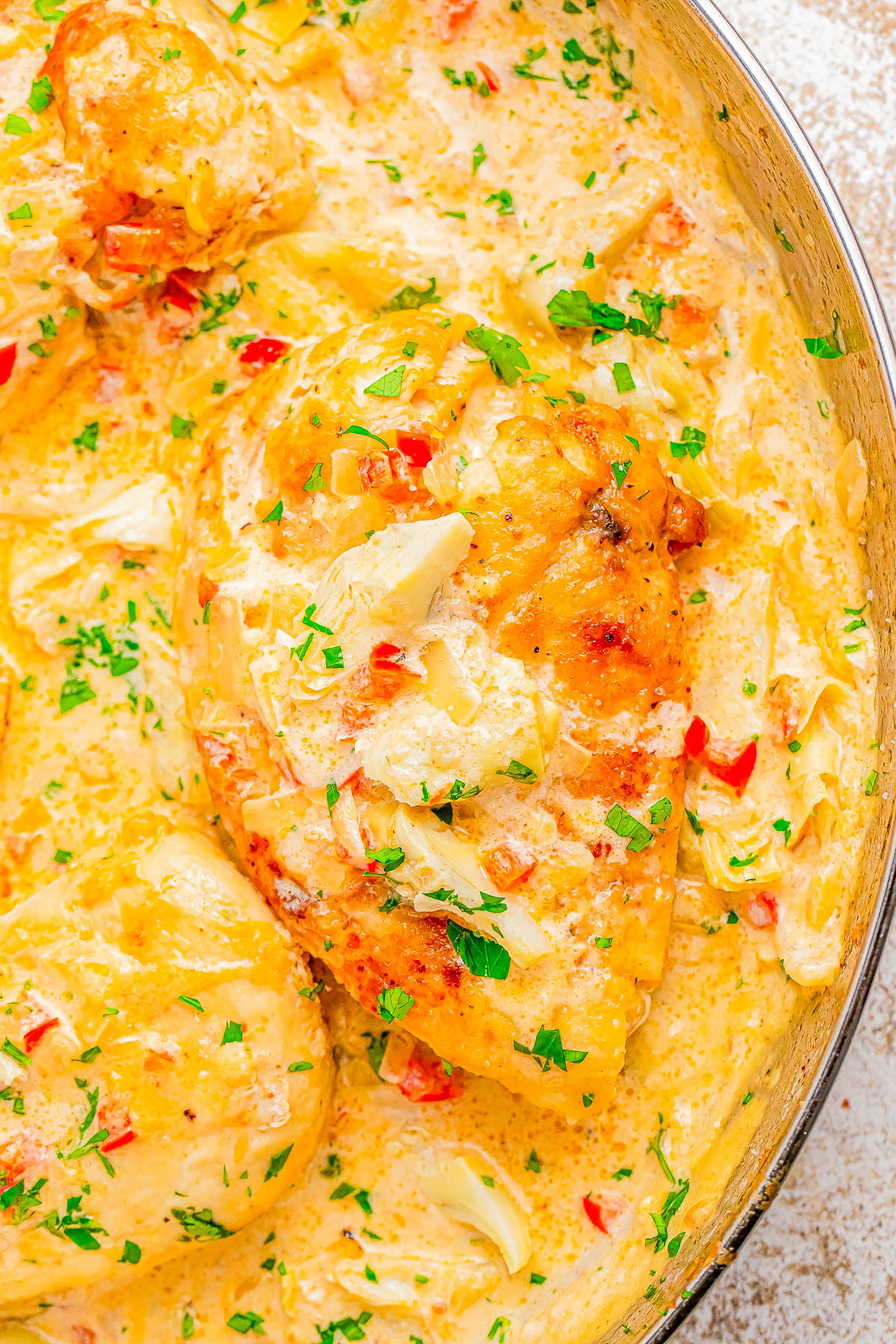 Creamy chicken breast dish garnished with chopped parsley and red peppers in a pan.