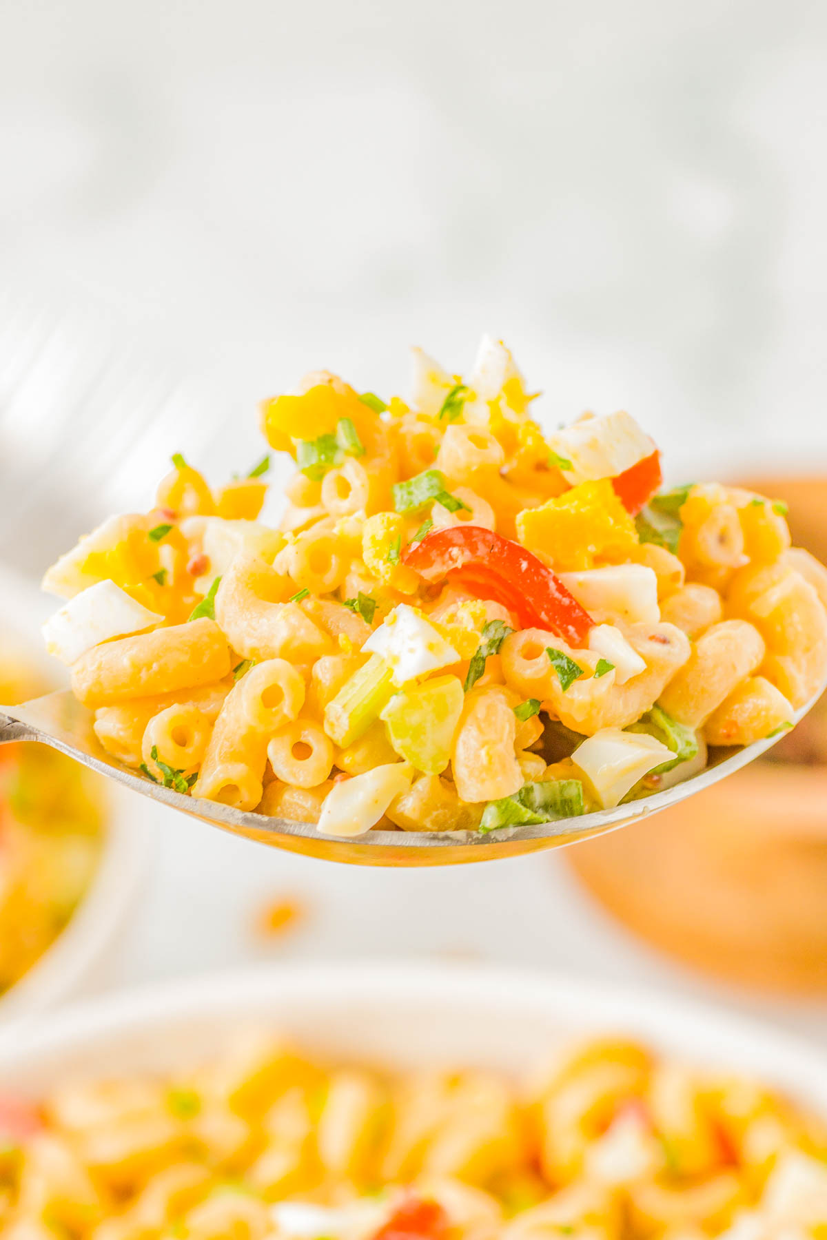 A spoonful of macaroni salad with diced vegetables, including peppers and onions, alongside small cubes of cheese.