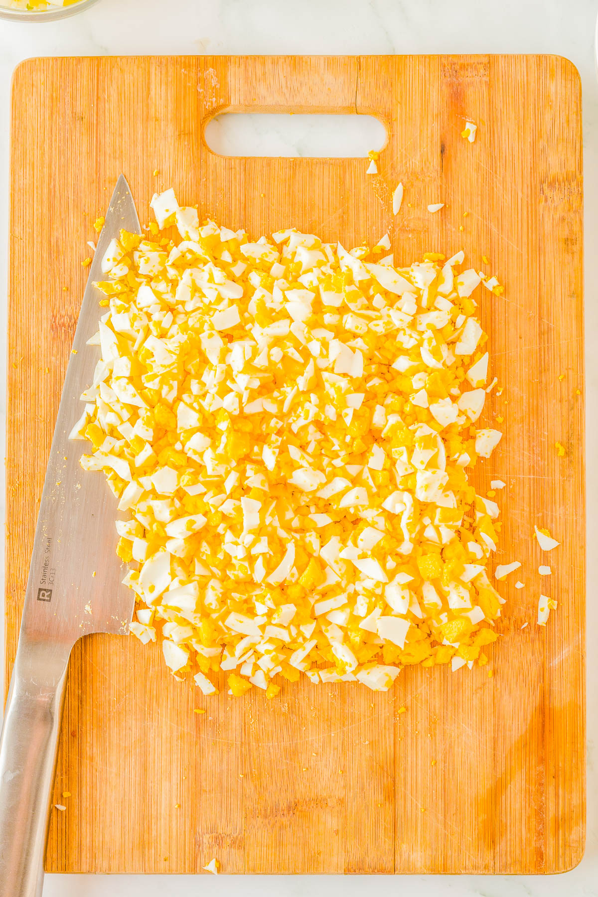 A cutting board with finely chopped hard-boiled eggs and a knife placed to the left.