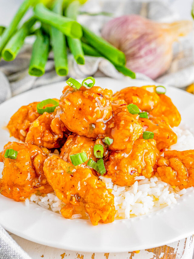 A plate of chicken with rice, garnished with green onions, surrounded by fresh green onions and a garlic bulb.