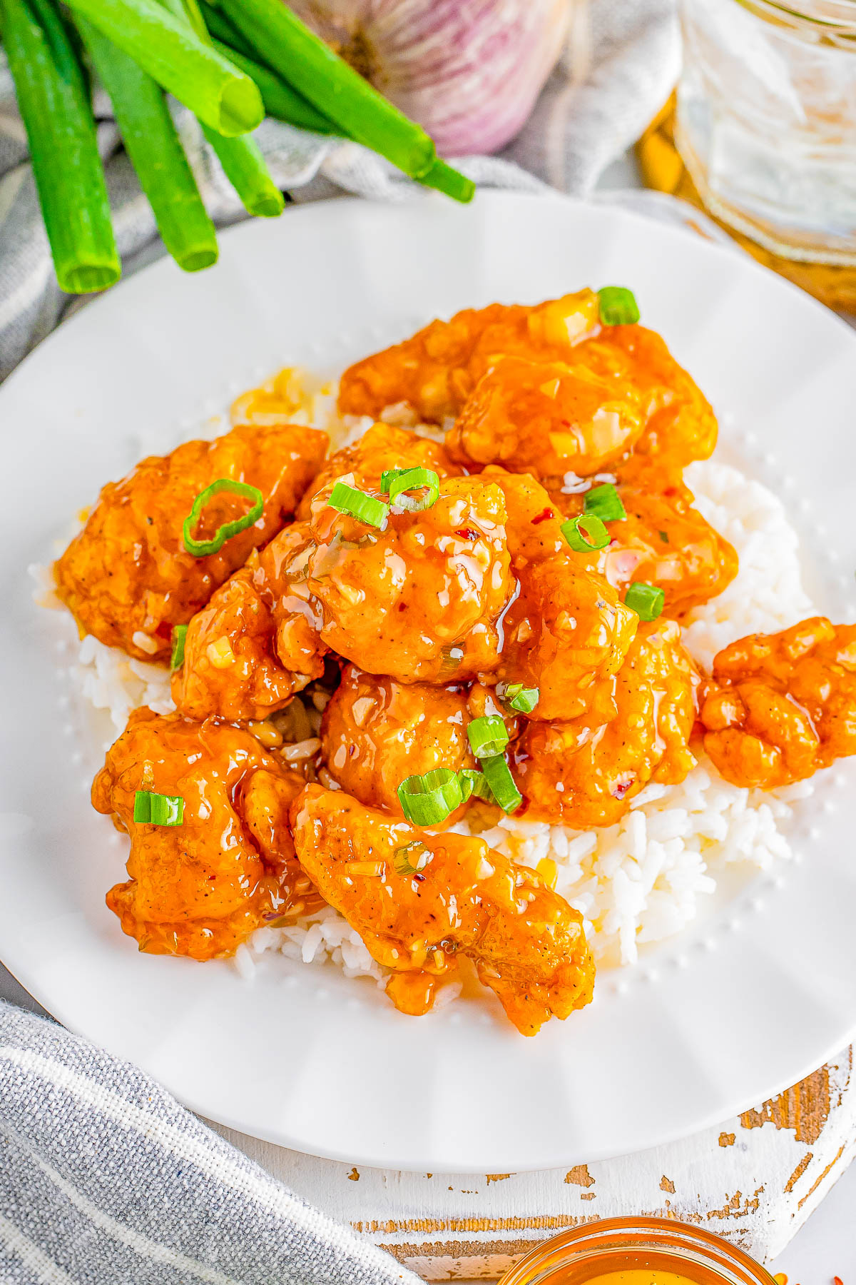 A plate of crispy chicken garnished with chopped green onions served on a bed of white rice.