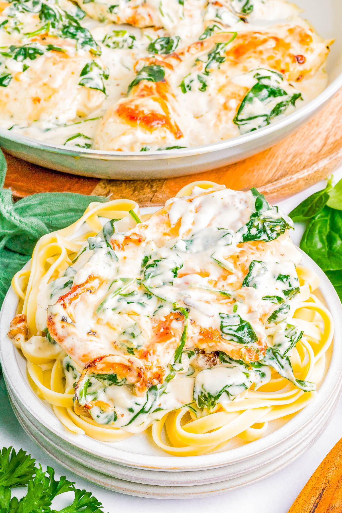 Plate of fettuccine pasta topped with a creamy spinach and cheese sauce, garnished with herbs. A serving dish of the same sauce is in the background.