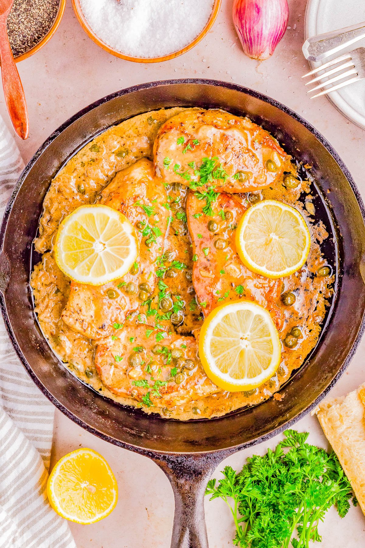 Lemon garlic chicken breasts in a skillet garnished with parsley, alongside ingredients and seasonings.