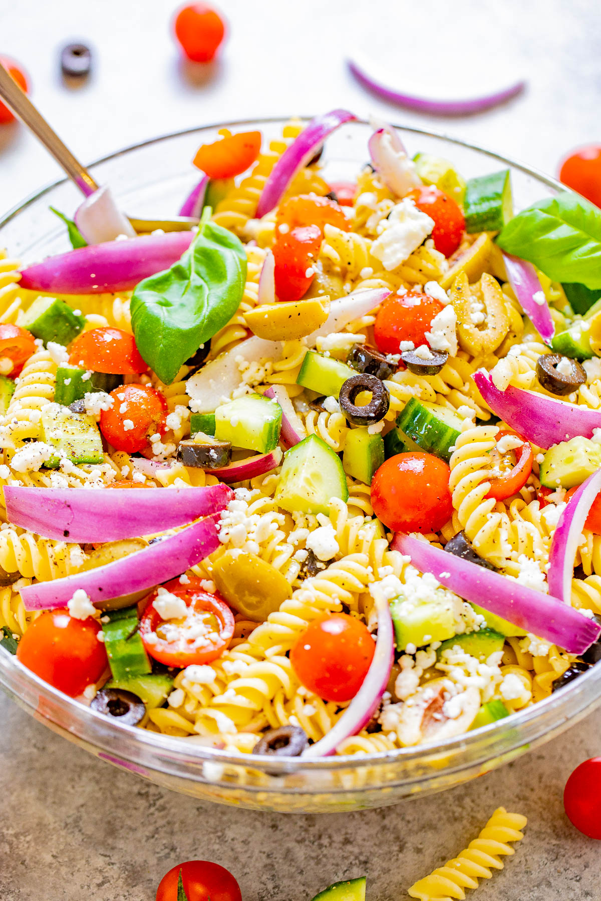 A bowl of creamy tuna pasta salad with rotini pasta, peas, and fresh parsley, placed on a light-colored surface.