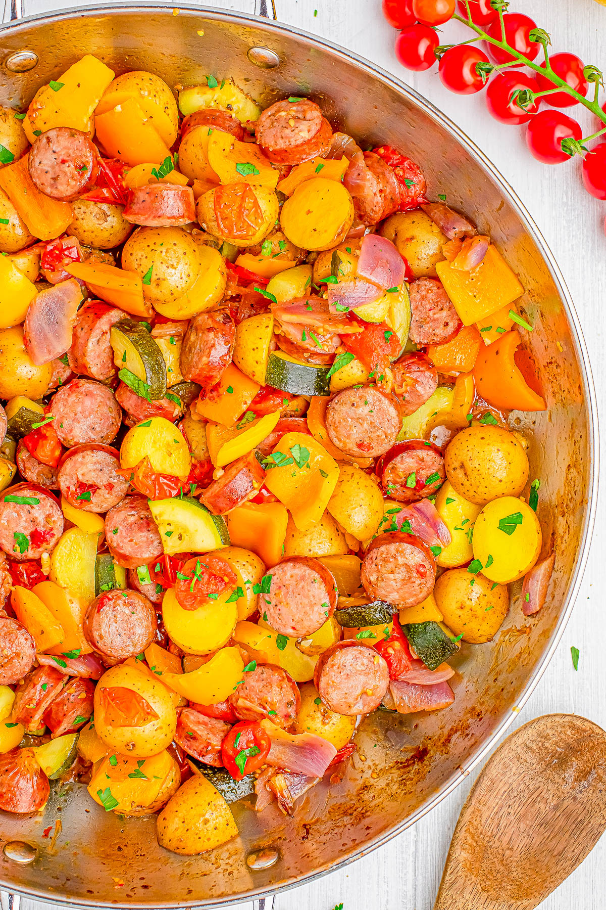 A skillet filled with cooked sausage, potatoes, bell peppers, onions, and herbs.