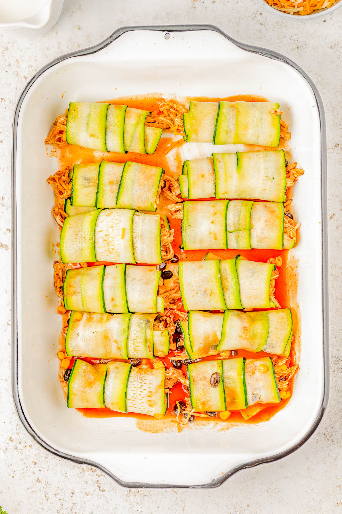 A baking dish contains 12 zucchini roll-ups filled with a mixture of shredded chicken and black beans, arranged in a grid pattern.