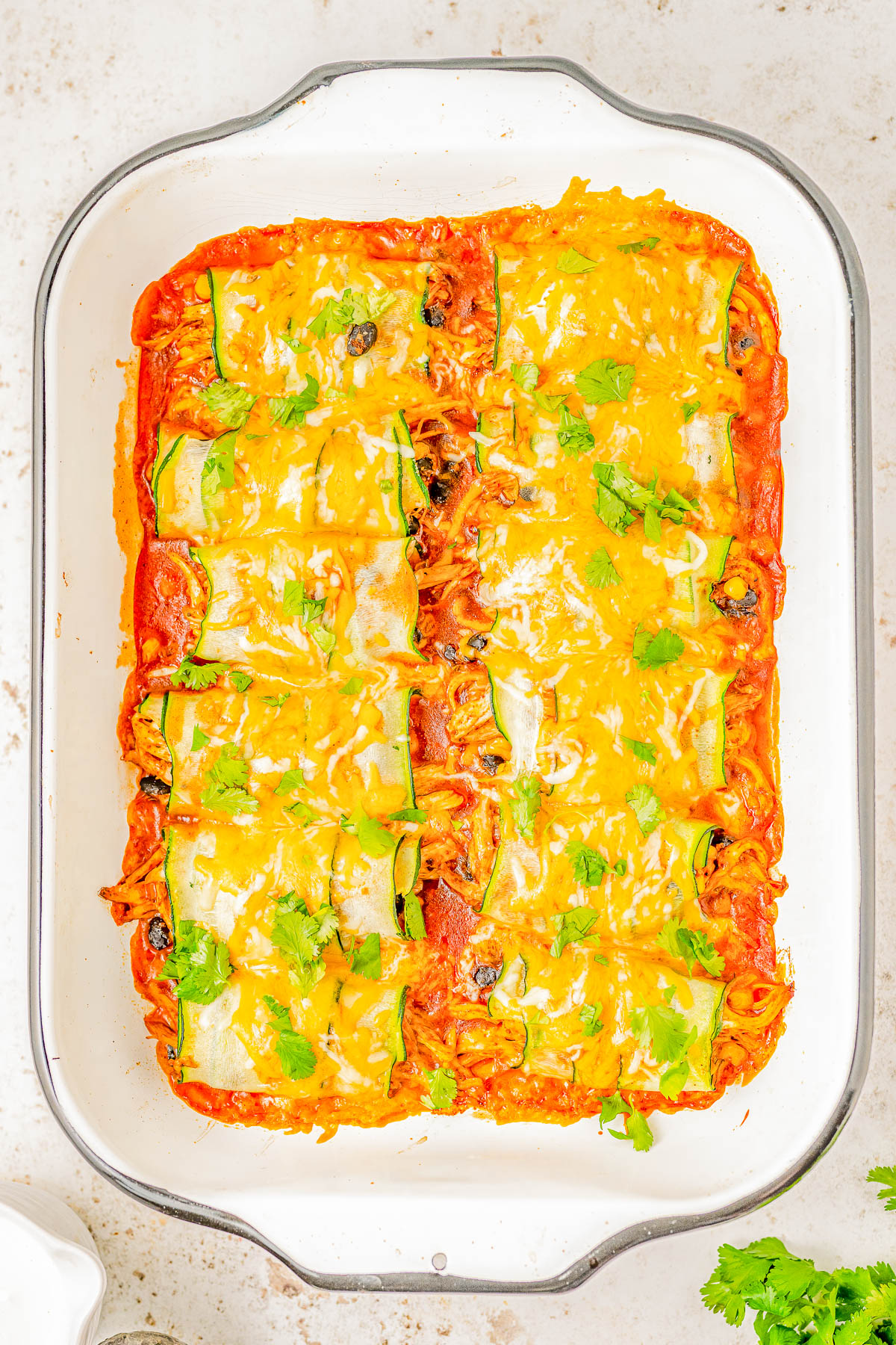 A baking dish filled with neatly arranged enchiladas topped with melted cheese and garnished with cilantro.