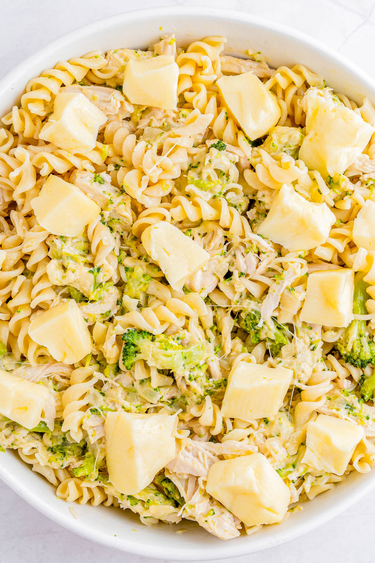 A bowl of rotini pasta mixed with broccoli and shredded chicken, topped with chunks of melted cheese.