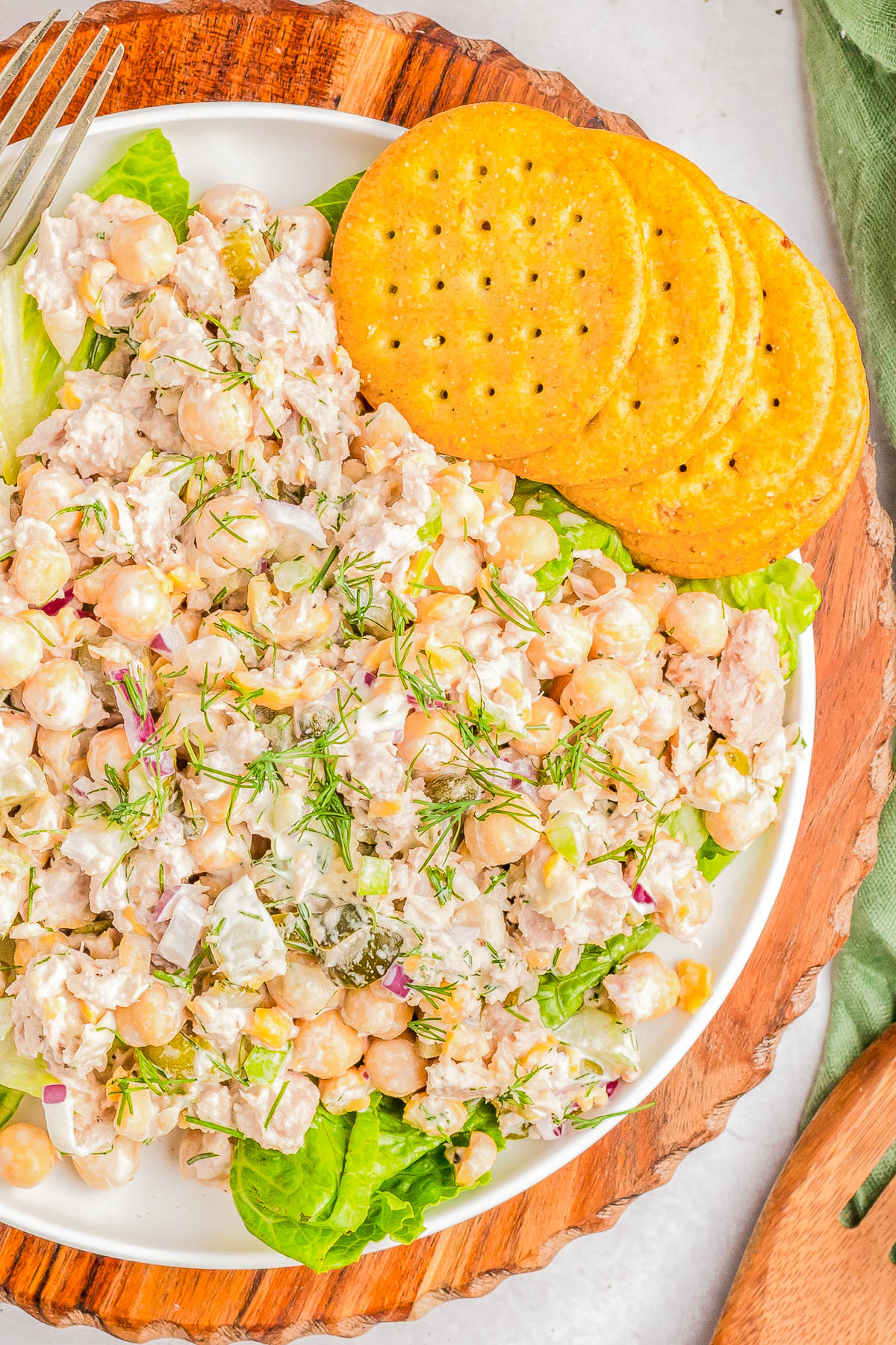 A plate of chicken salad with chickpeas, diced vegetables, and herbs, served on a bed of lettuce with several round crackers on the side.