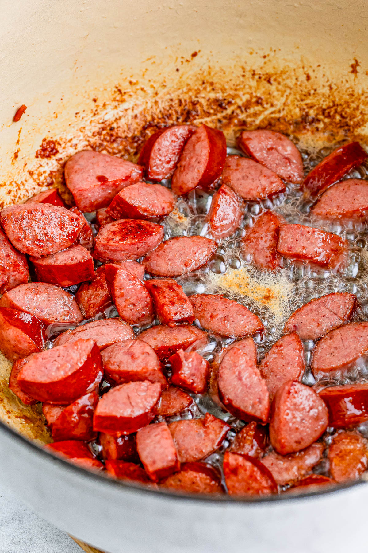 Sliced sausage pieces being fried in a skillet with visible browned bits and sizzling oil.