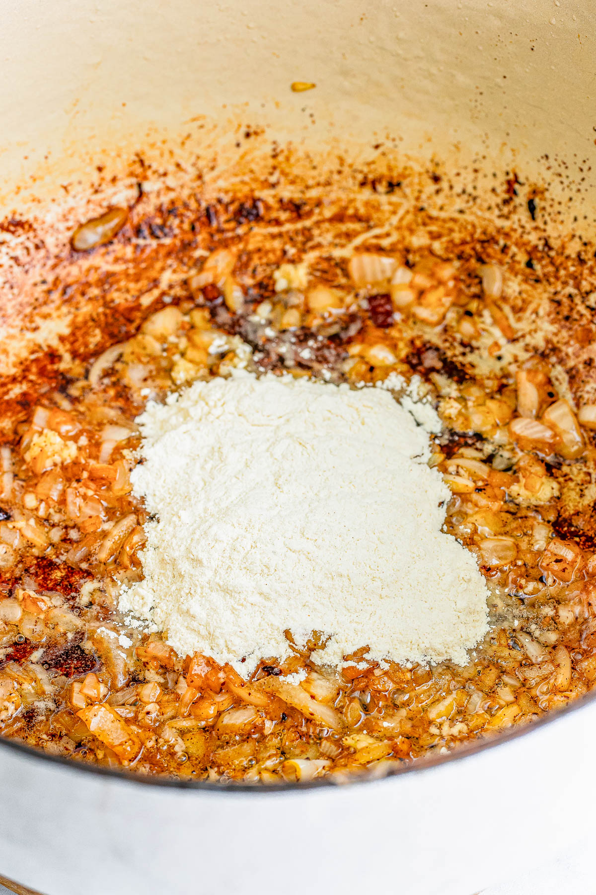 Chopped onions being sautéed in a pot with a mound of flour added, surrounded by a light brown, caramelized mixture.