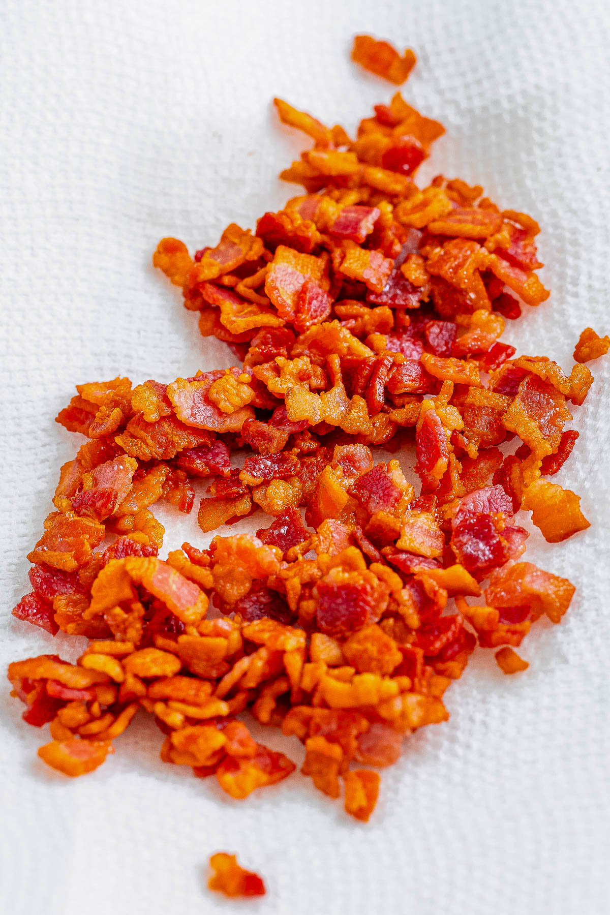 Crispy, chopped bacon pieces are laid out on a white paper towel.