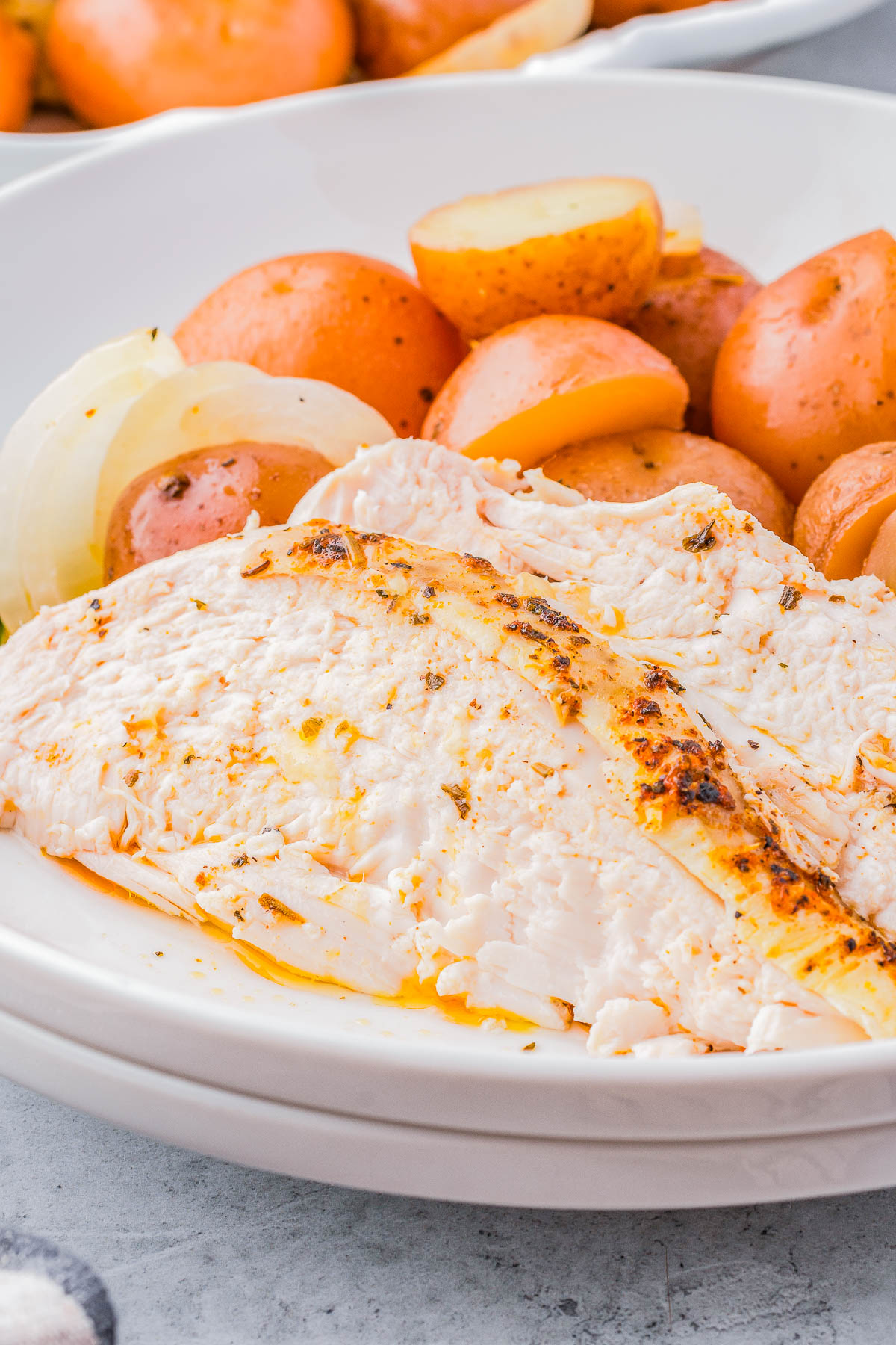 A plate with seasoned, cooked chicken, accompanied by sliced boiled red potatoes and white onions.