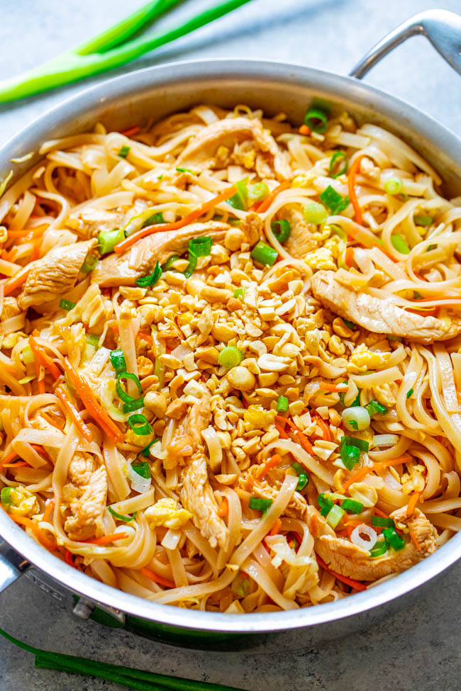 Stir-fried noodles with chicken, carrots, and green onions, garnished with crushed peanuts.