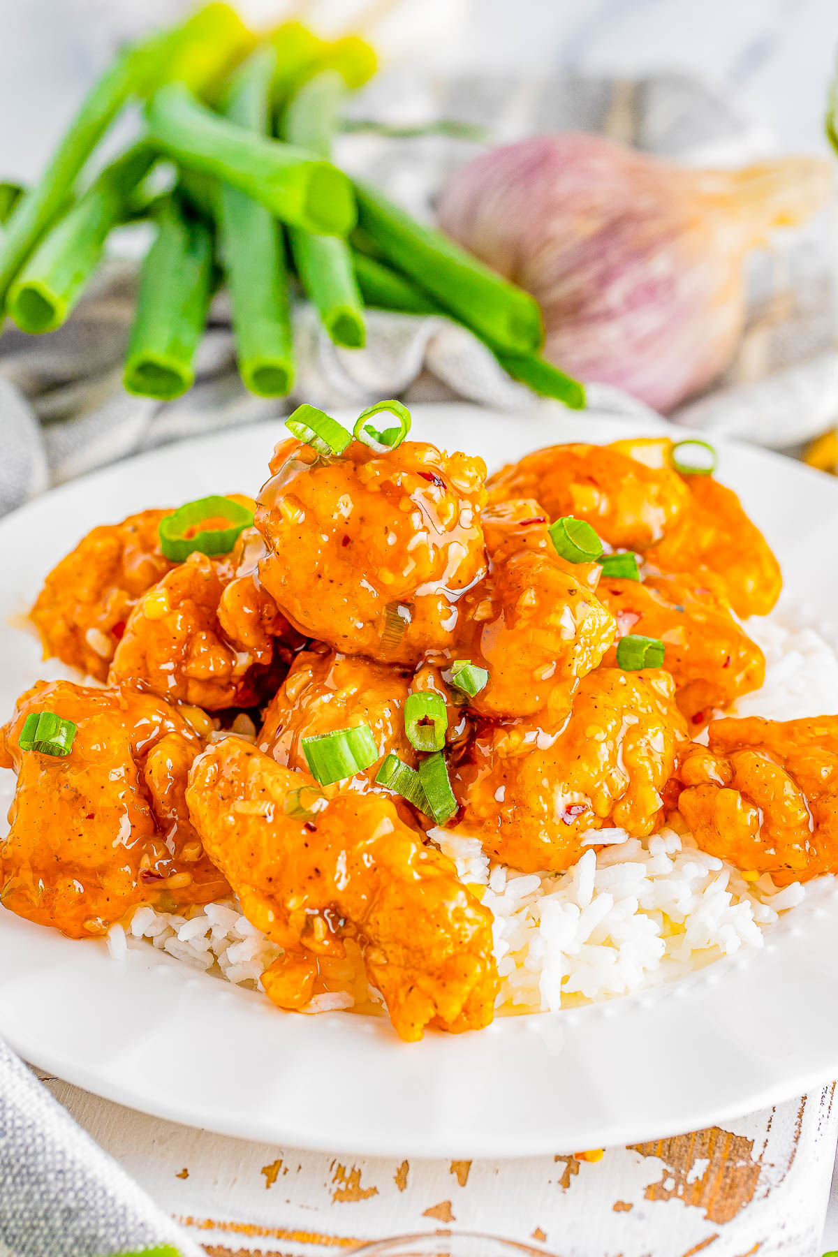 A plate of chicken with rice, garnished with green onions, surrounded by fresh green onions and a garlic bulb.