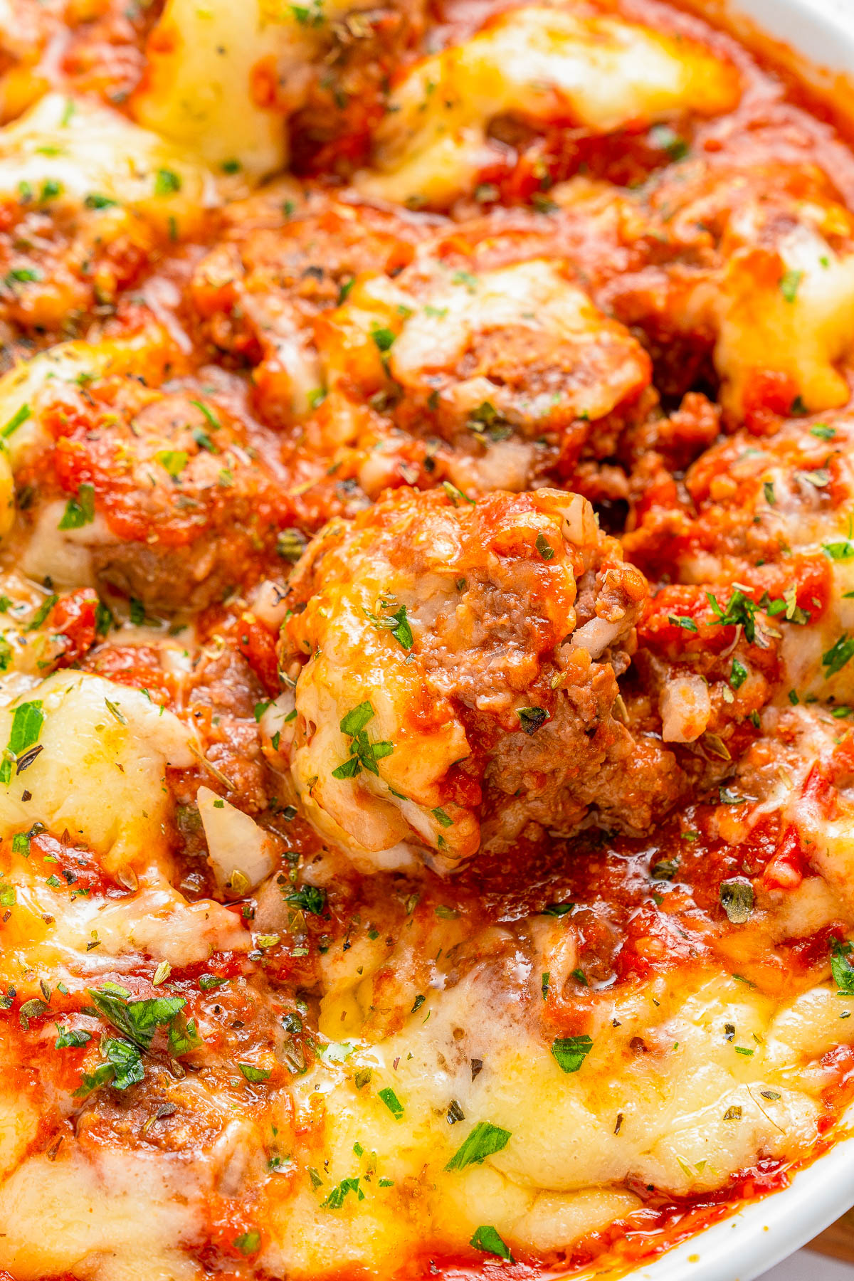 Close-up of a baked dish featuring meatballs covered in marinara sauce and melted cheese, garnished with chopped parsley.