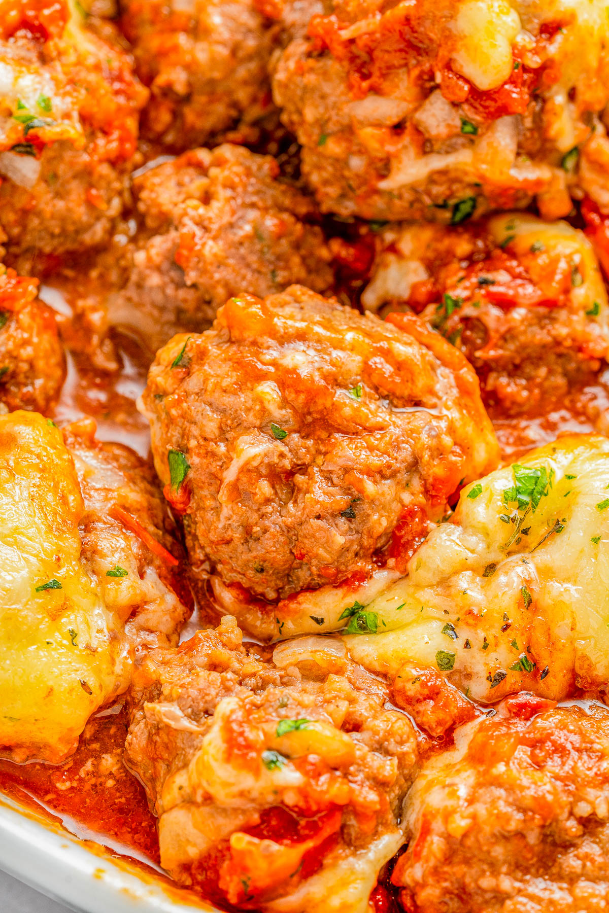 Close-up of cheesy meatballs covered in marinara sauce, garnished with herbs.