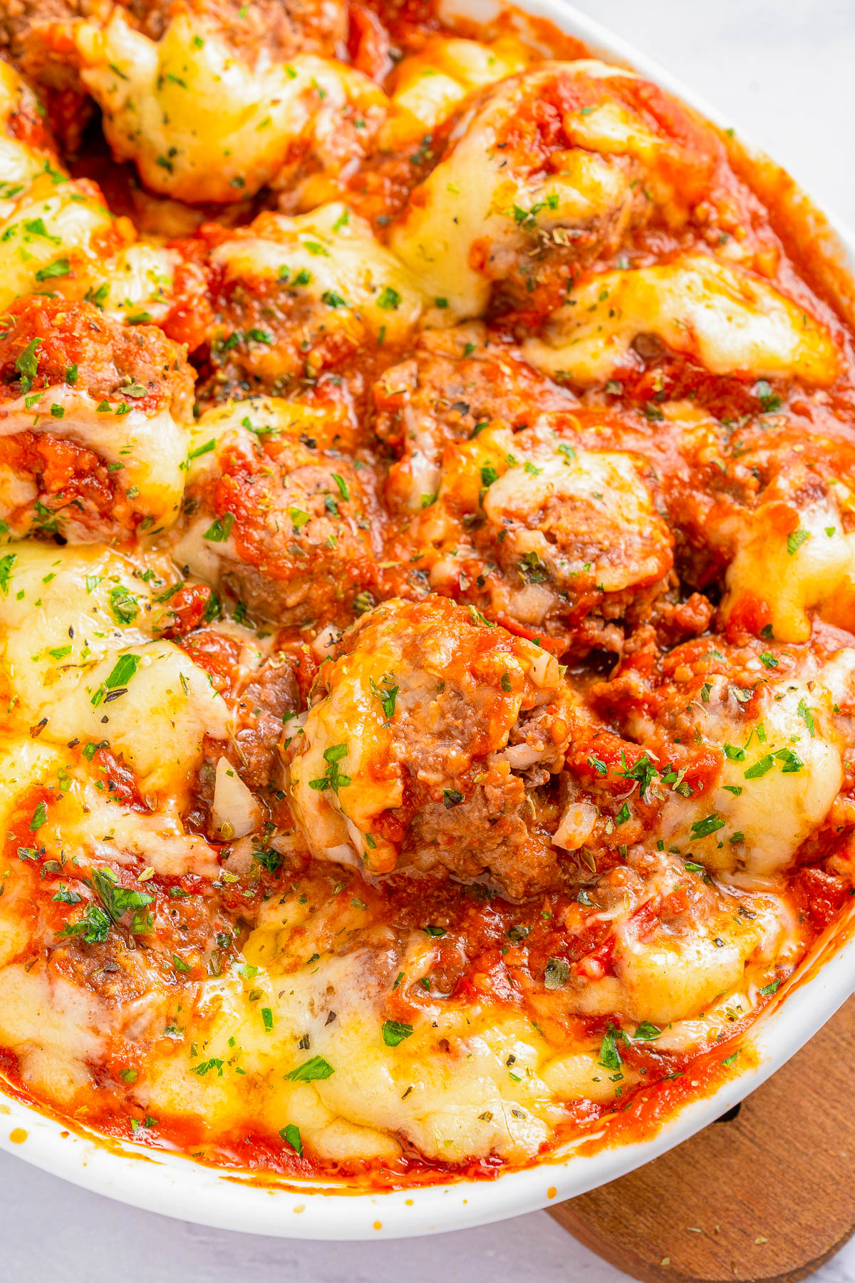 A close-up of a baked dish featuring meatballs covered with melted cheese, marinara sauce, and garnished with chopped herbs.