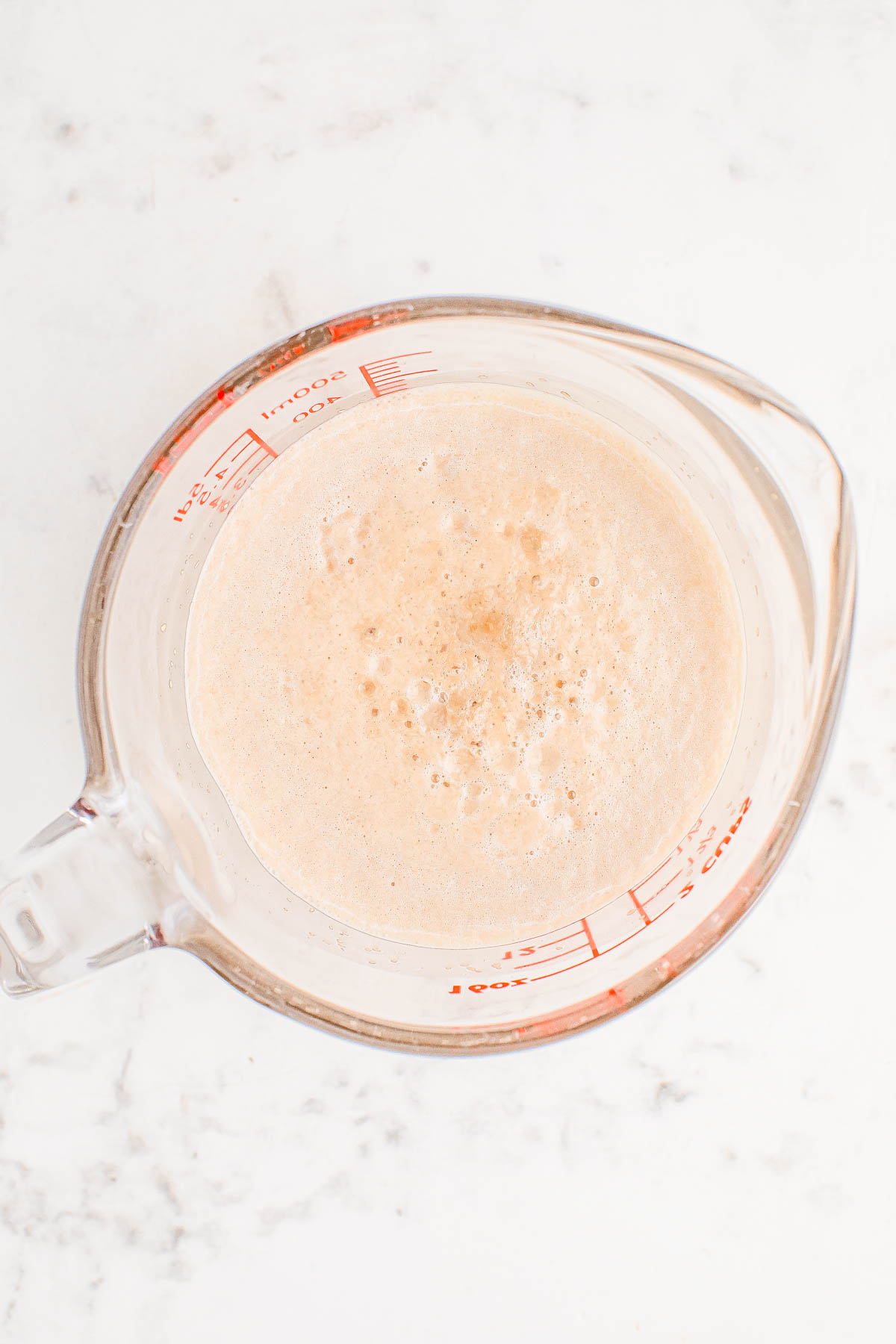 A measuring cup filled with blended frothy liquid, placed on a marble surface.