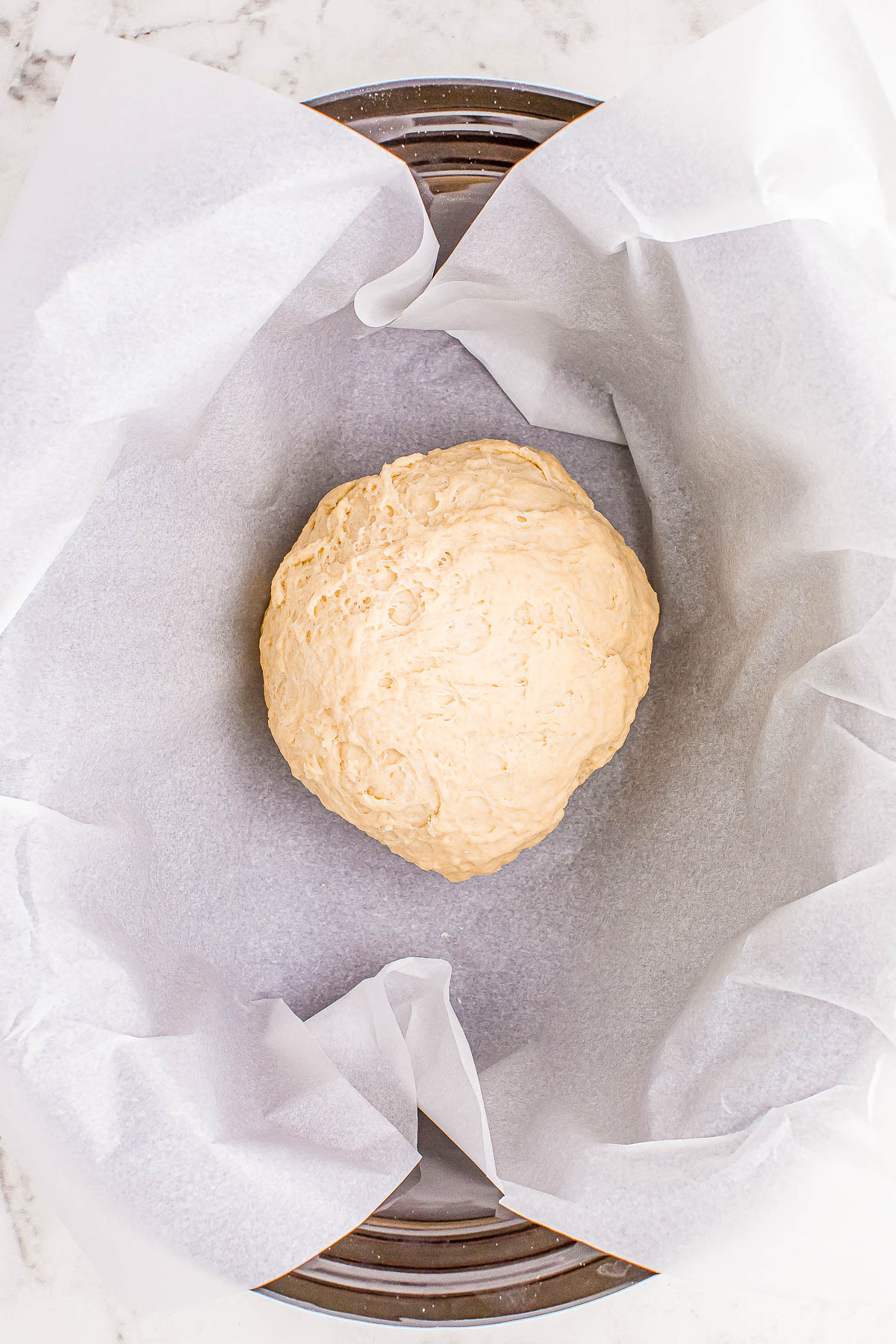 A ball of dough placed on parchment paper in a round baking pan, ready to be baked.