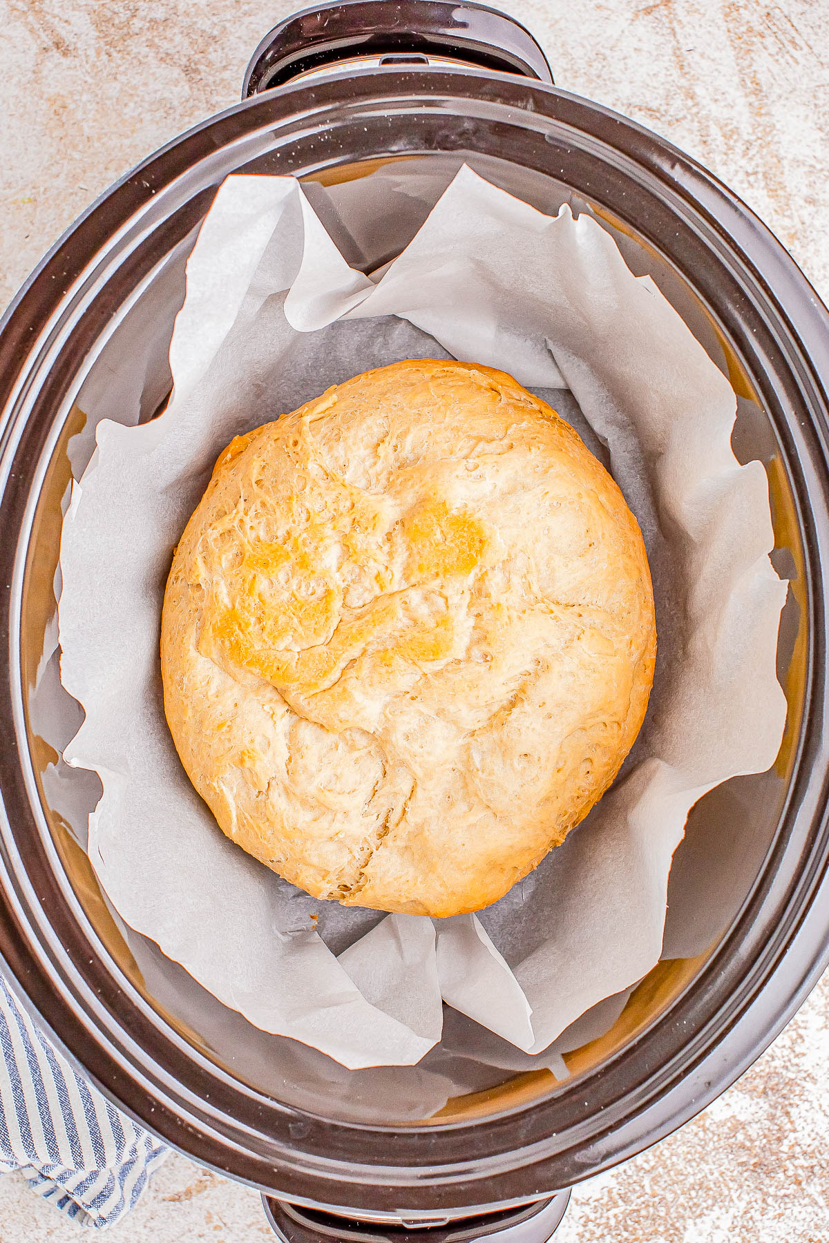 A loaf of bread on parchment paper inside a crock pot.