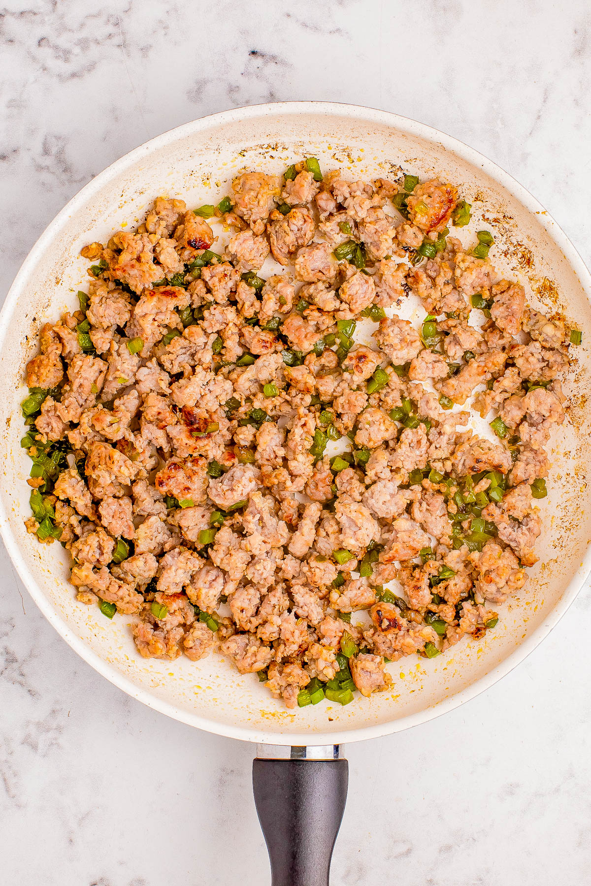 A frying pan containing browned ground meat mixed with chopped green vegetables on a marble countertop.