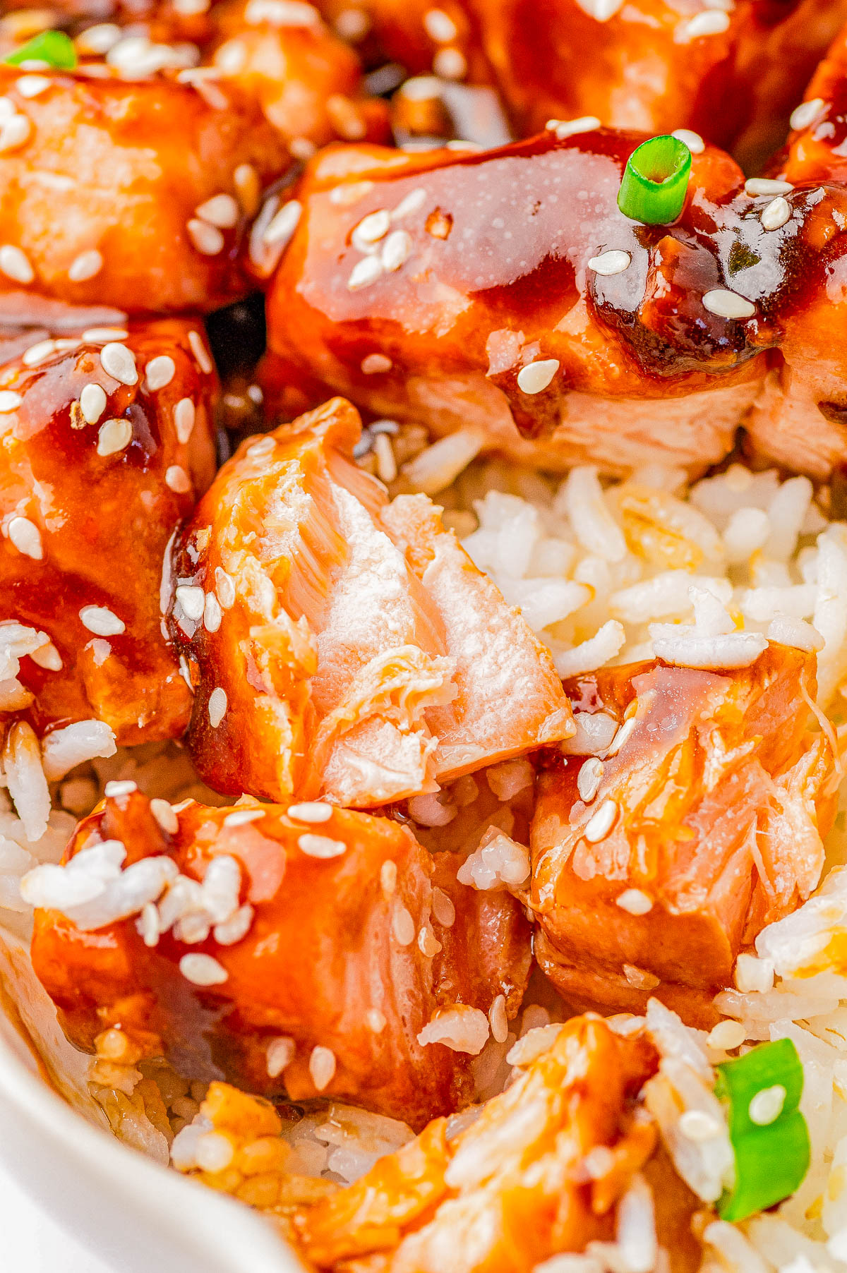 Close-up of teriyaki chicken on a bed of white rice, topped with sesame seeds and garnished with a small piece of green onion.