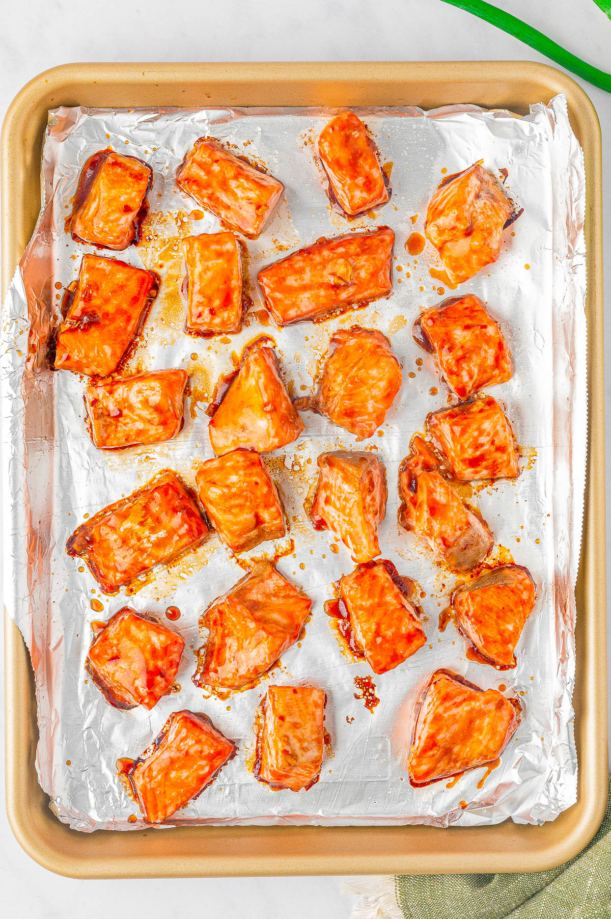 A baking tray lined with aluminum foil containing several pieces of cooked salmon glazed with a sticky sauce.