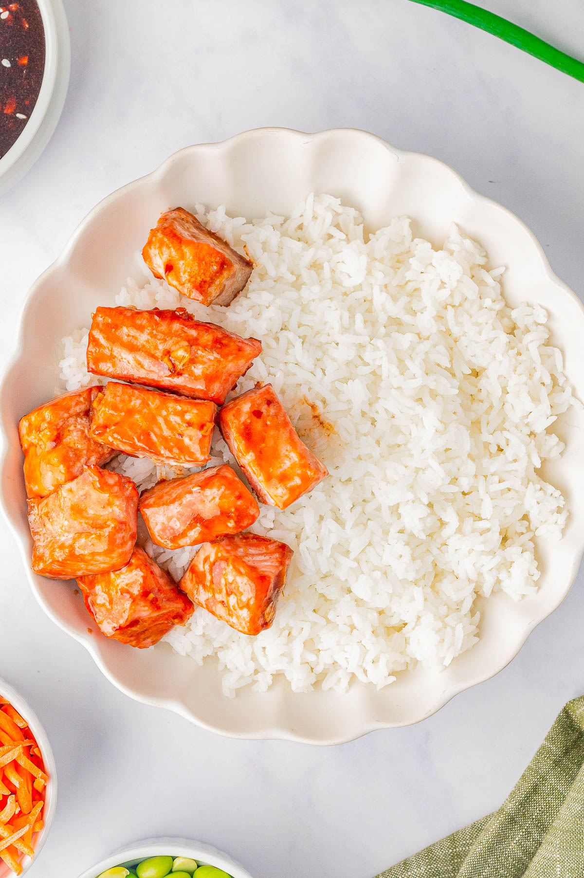 A plate with white rice and pieces of orange-glazed salmon.