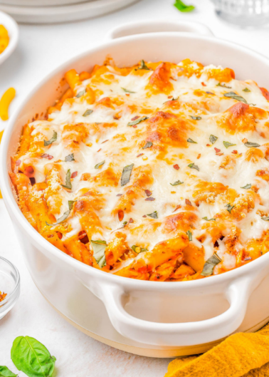 A white casserole dish filled with baked ziti pasta topped with melted cheese and garnished with herbs.