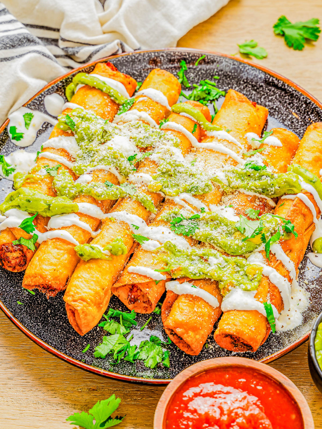 A plate of crispy taquitos topped with green sauce, cream, crumbled cheese, and garnished with fresh cilantro. A small bowl of red sauce is in the foreground.