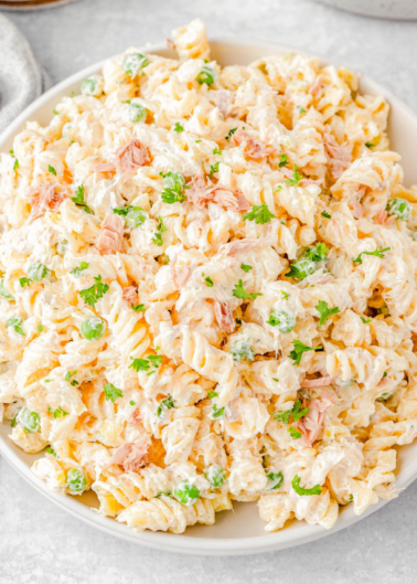 A bowl of rotini pasta salad with peas, shredded chicken, chopped parsley, and a creamy dressing.